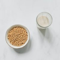 top view photo of soybeans on bowl near drinking glass with soy milk